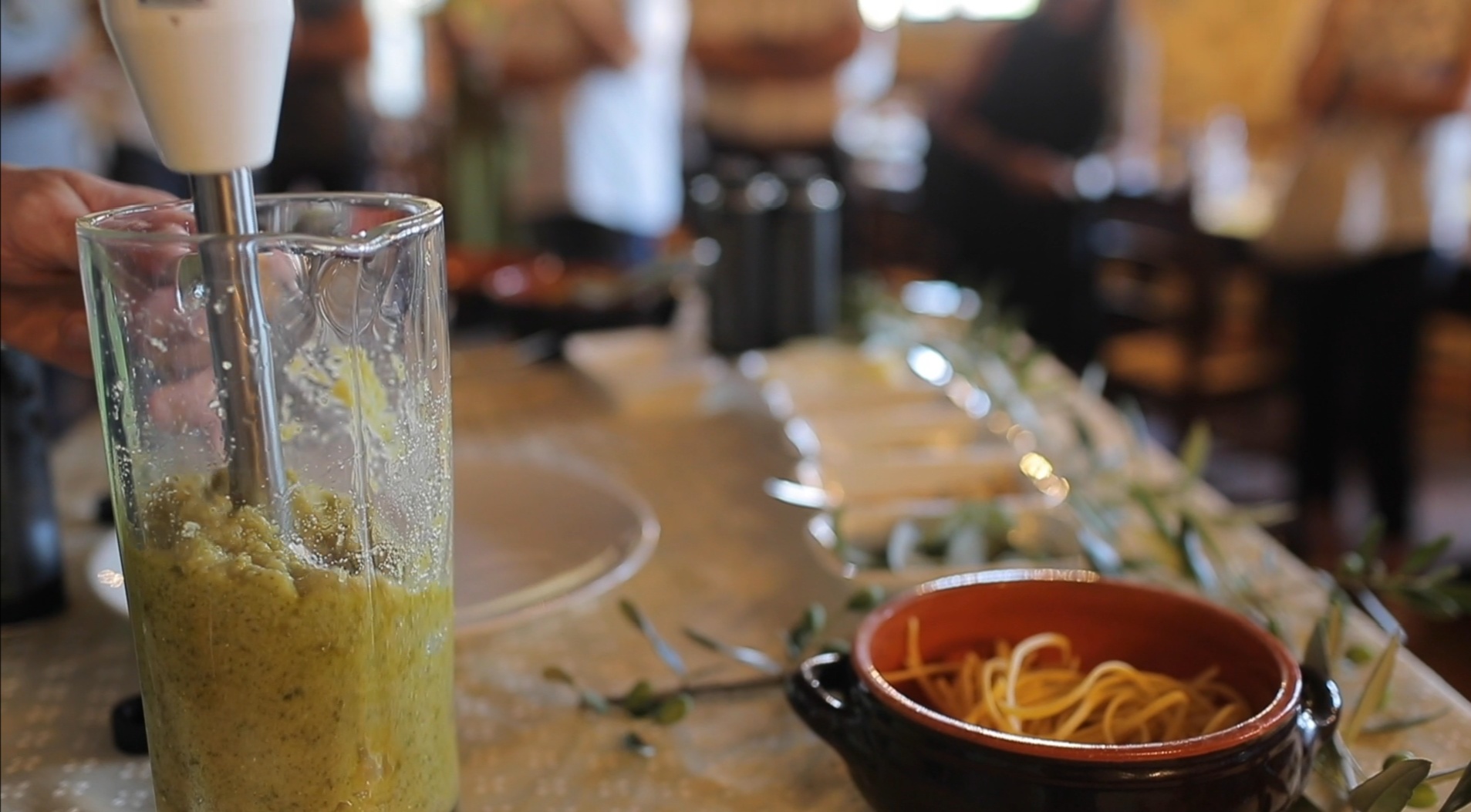 Tavolo con recipiente pieno di pesto, piatto di spaghetti, utensili